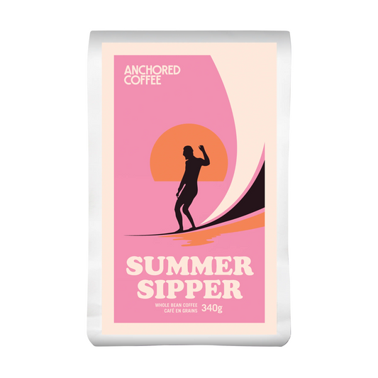 Anchored Coffee Summer Sipper 340 g bag standing upright on a wooden surface.
The packaging features a bright pink label with Anchored’s logo and seasonal design.
