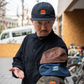 Blue Lug House Logo cap in black, being worn by a man showing other colours of the cap on his arm