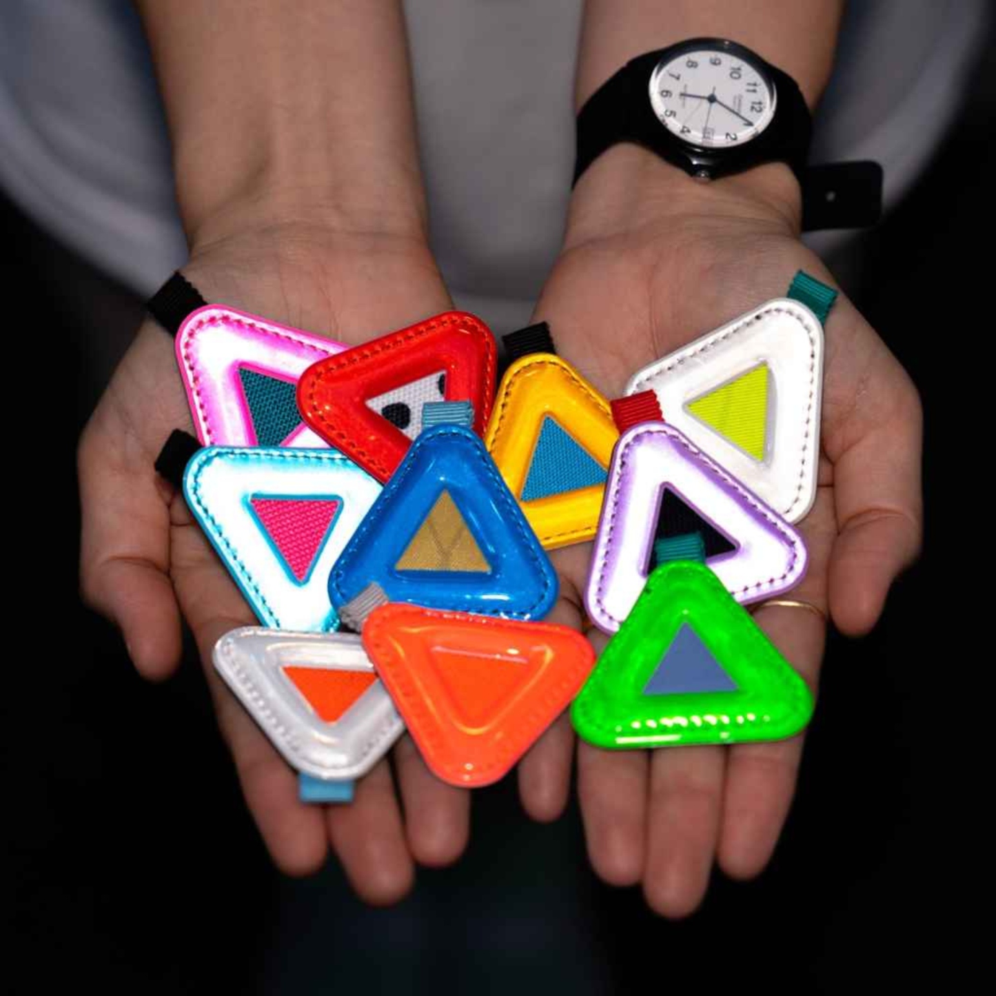 Blue Lug Mini Triangle Reflectors in assorted colours being held in hands with flash photo showing reflectiveness