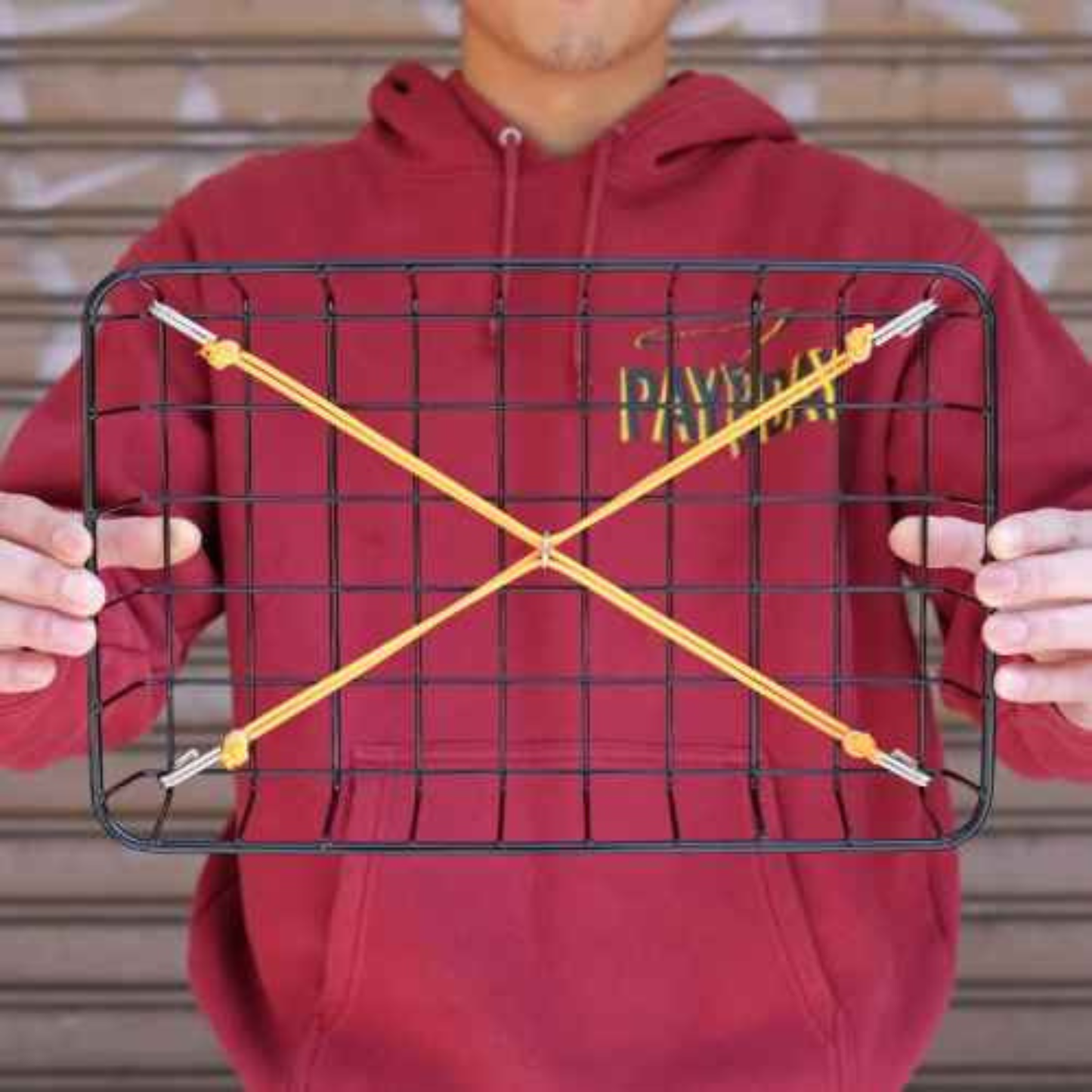 Blue Lug X-Strap elastic cargo strap in orange colour, shown installed on basket being held by someone