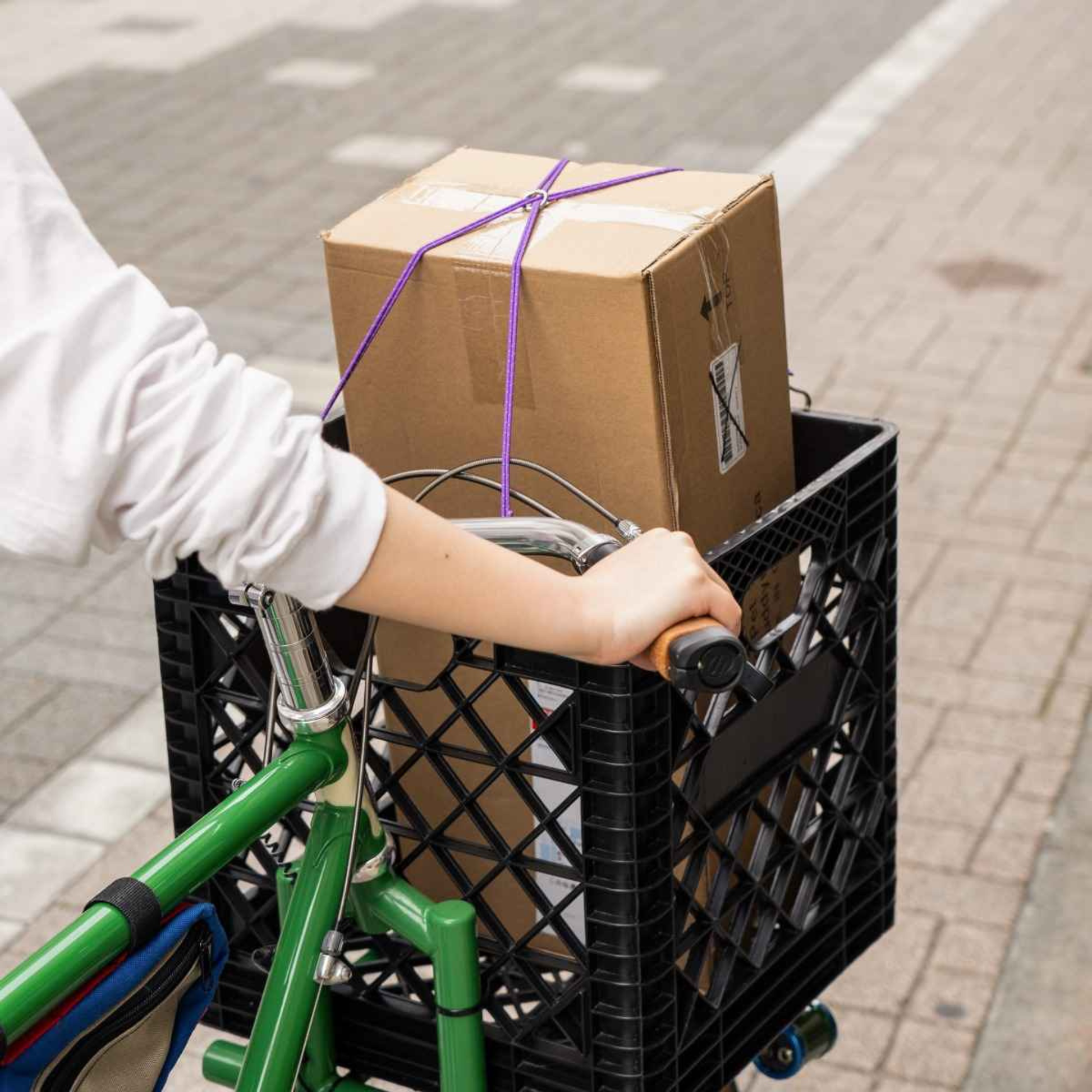 Blue Lug X-Strap elastic cargo strap in purple colour securing a box in a milk crate on bicycle