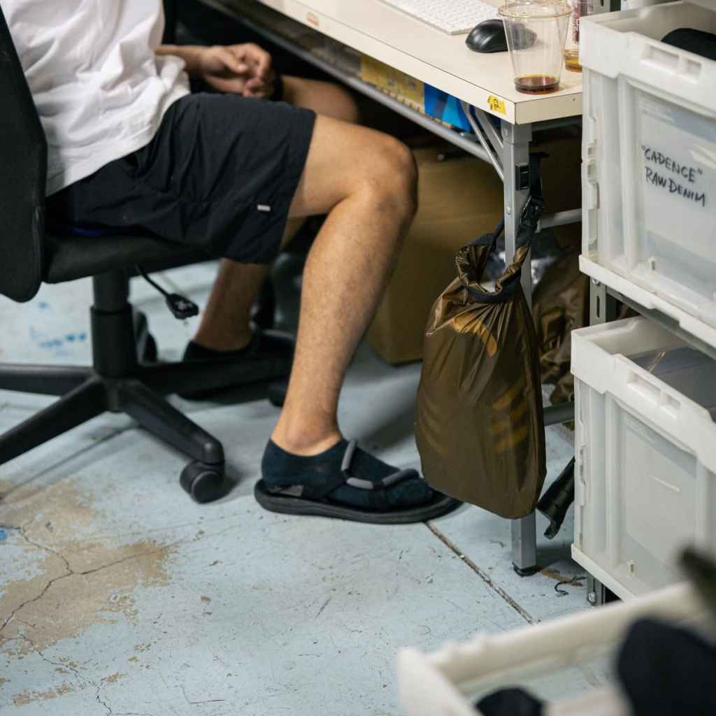 Person sitting on a chair with legs crossed, in an office with a coyote brown Fairweather Dry Sack attached to their desk