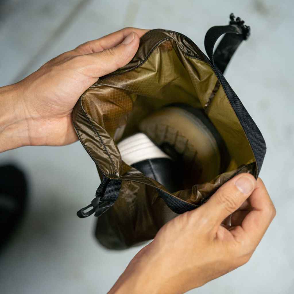 Person holding a coyote brown Fairweather Dry Sack , containing a pair of shoes.