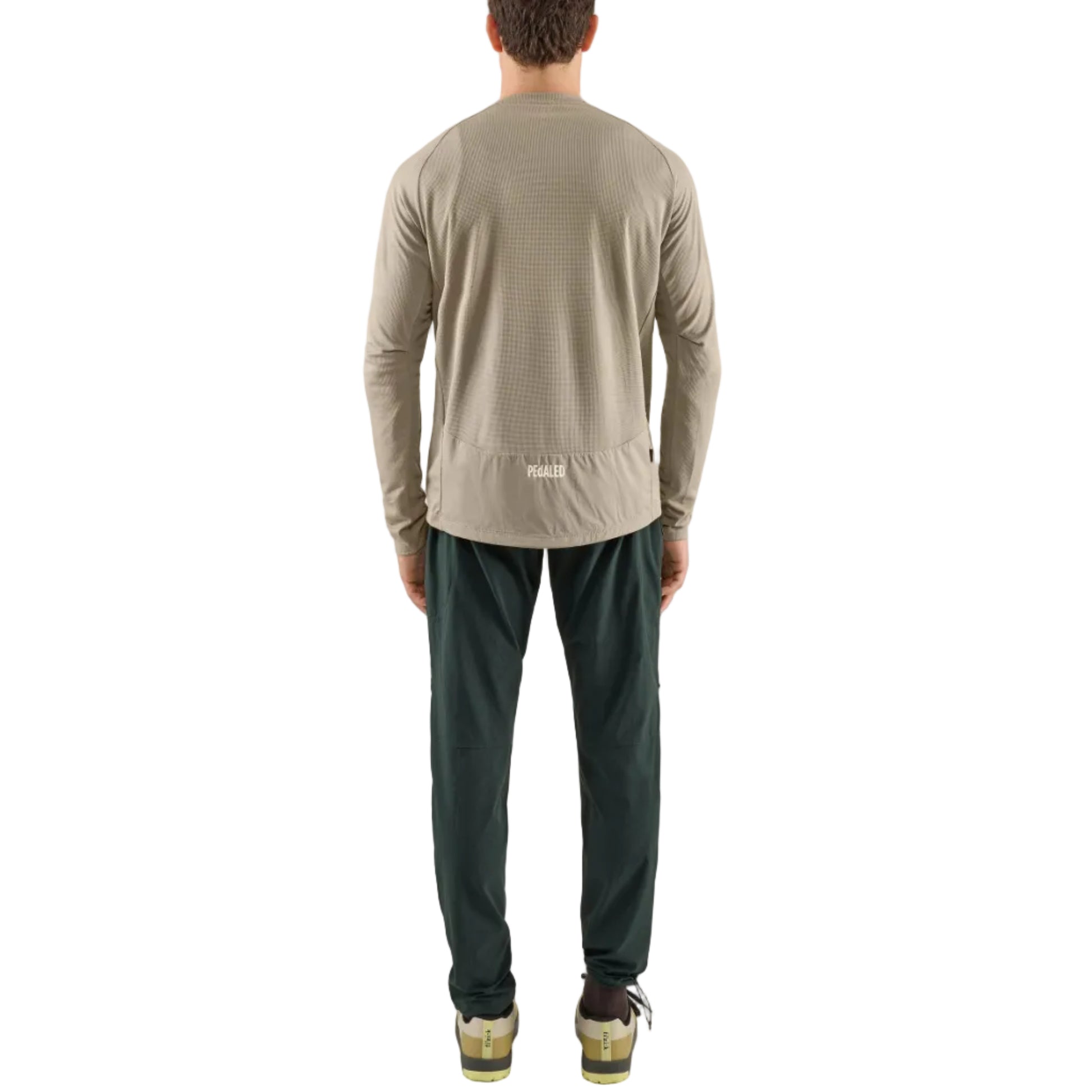 Man wearing a pedaled beige long-sleeve tech jersey shirt and Yuma Trail Pants dark pants on a light gray background