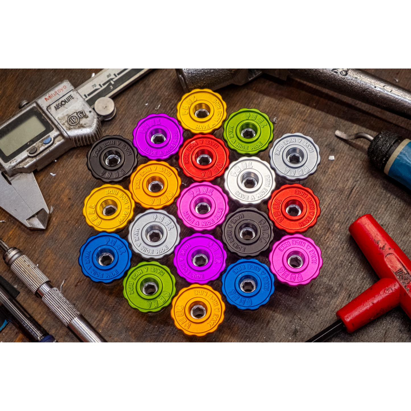 A collection of the Paul Bar End Caps arranged in a circle on a wooden surface, surrounded by various hand tools including calipers, a hex key, and a drill bit.