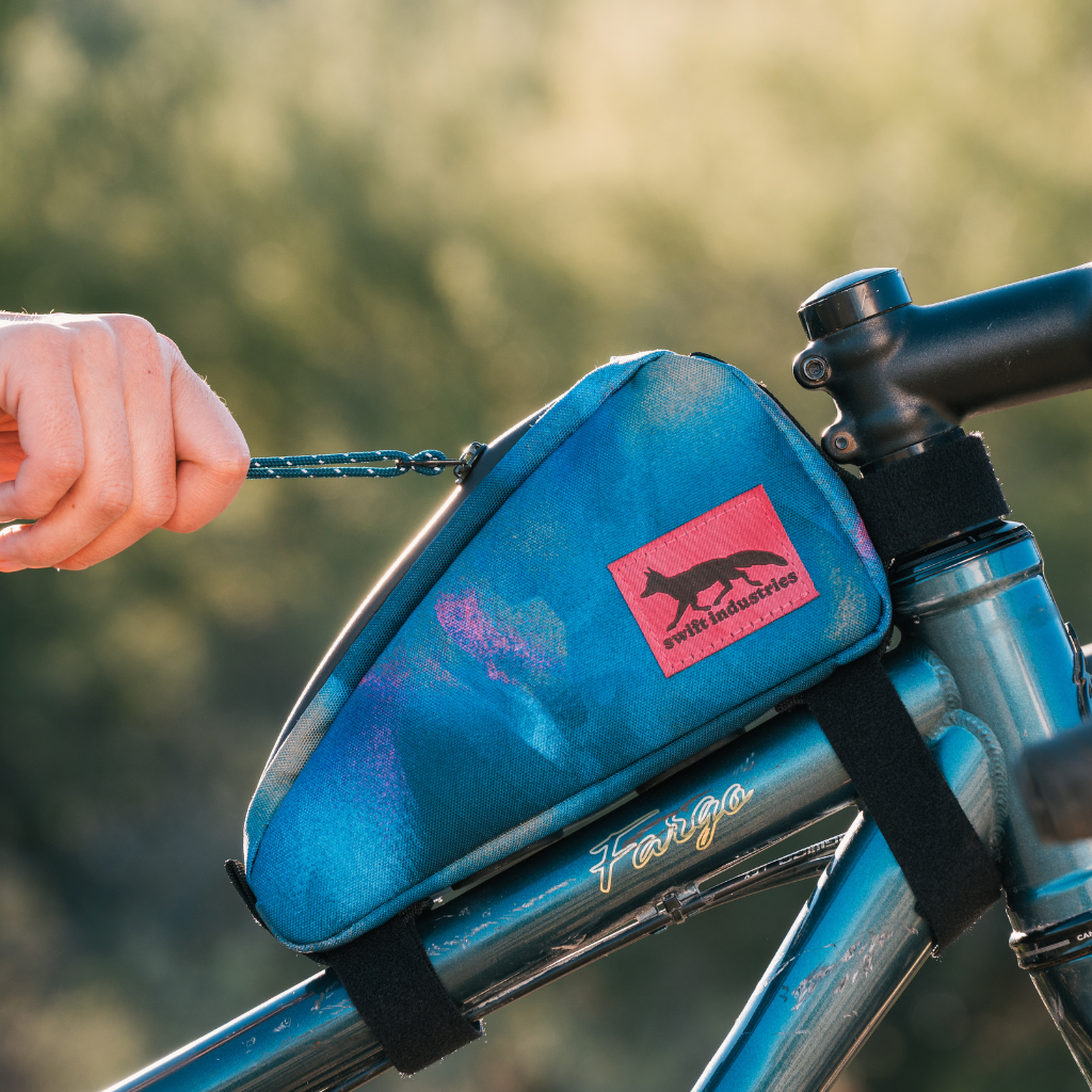 Swift Industries Luminary Moxie Top Tube Bag mounted on a bicycle with the zipper being pulled by a human hand 